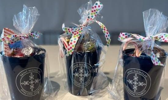 Black Mugs With St. Nick's Logo In White, Filled With Candy And Wrapped In Clear Cellophane And Ribbons.