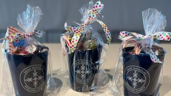 Black mugs with St. Nick's logo in white, filled with candy and wrapped in clear cellophane and ribbons.