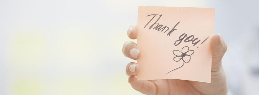 Hand with painted nails holding up a note that has "Thank you!" written on it, with a flower drawn beneath it.