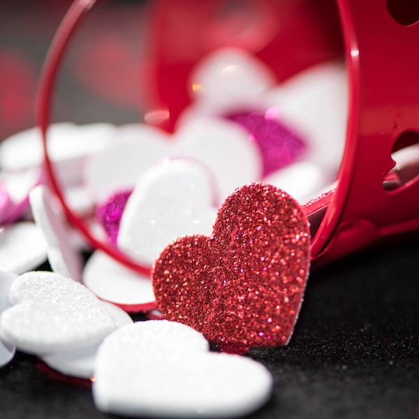Valentine heart decorations spilling out of small red tin bucket with hearts cut into it