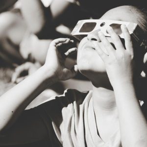 black and white photo with a child with solar eclipse glasses on looking upward