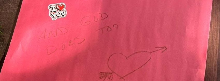 A pink piece of paper with a sticker on it that says, "I love you," and writing that says, "and God does too" along with a heart, underneath the sticker.